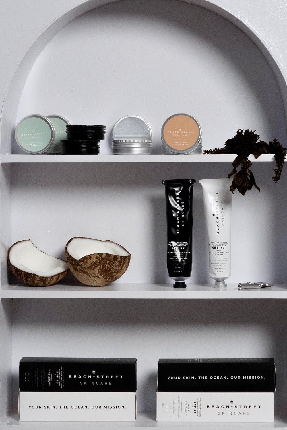 Cosmetic products on a white shelf with coconuts and decorative elements.