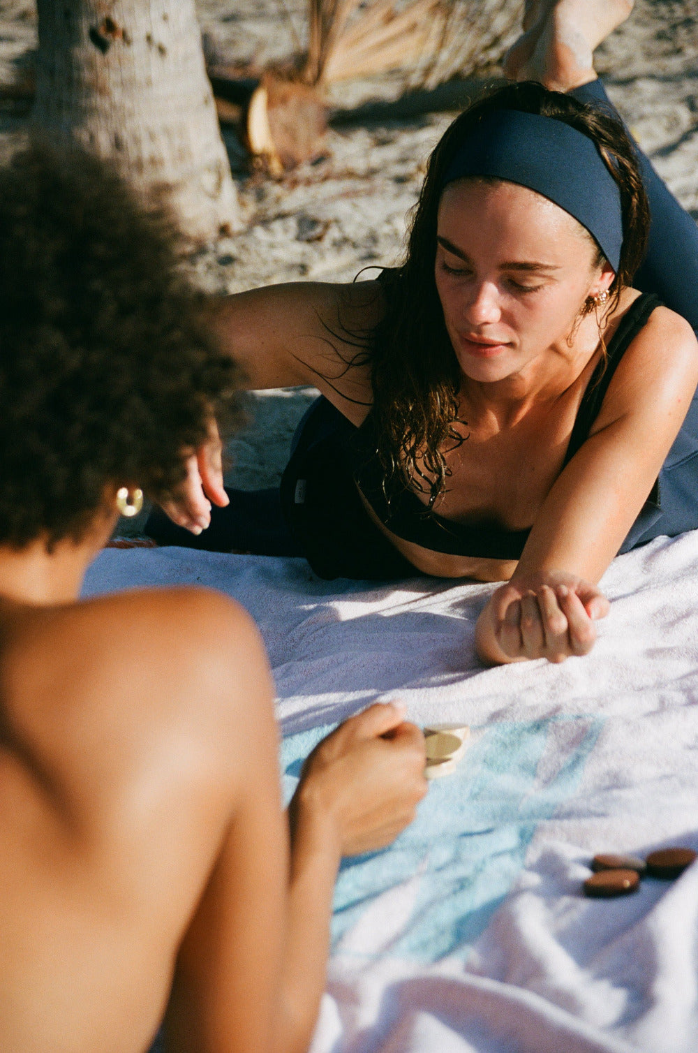 Two women lying on a towel at the beach with palm trees in the background