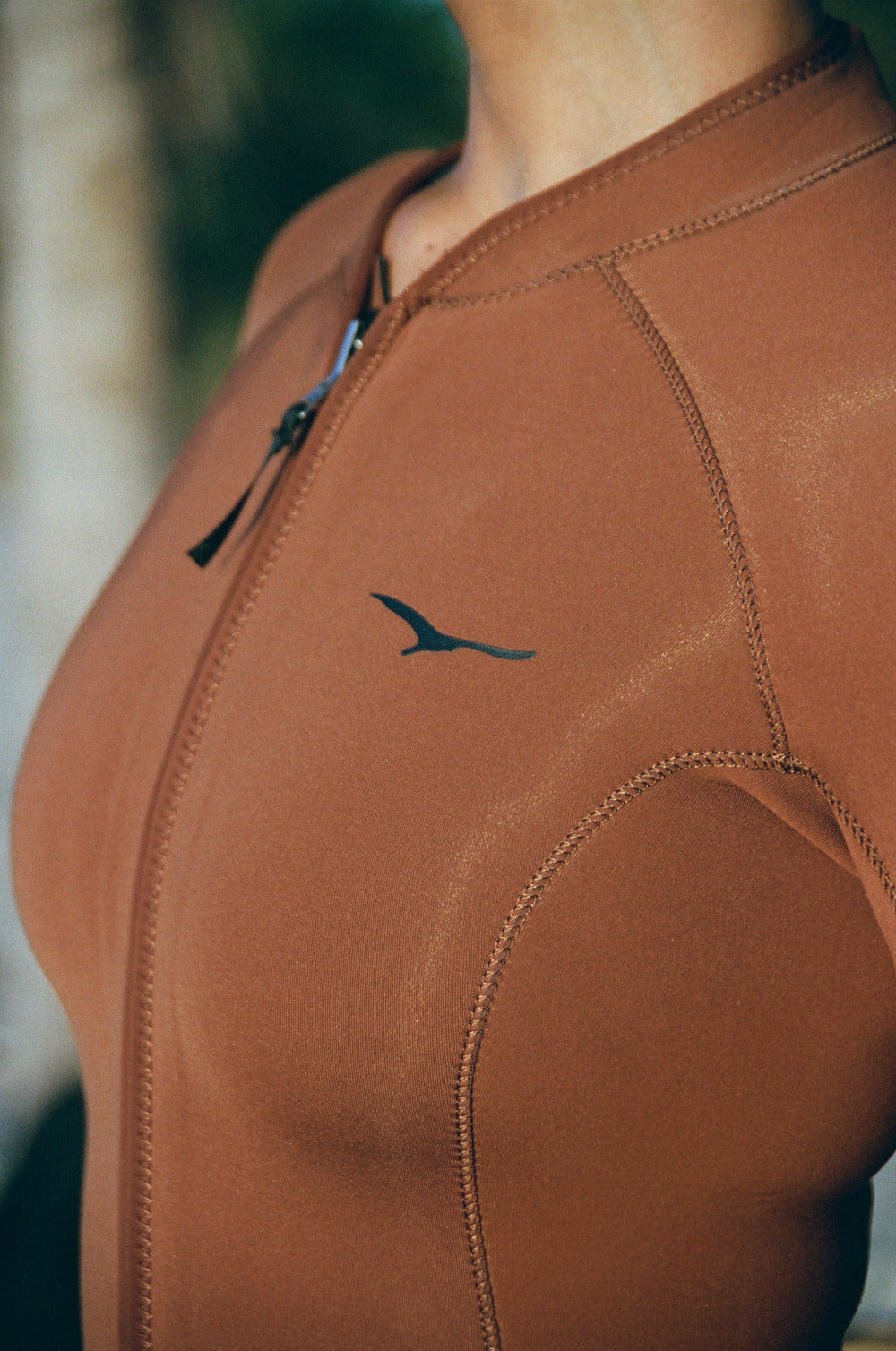 Close-up of a brown wetsuit with a logo on a blurred natural background