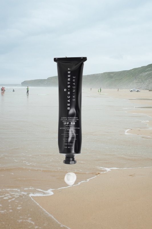 Black tube of sunscreen on a sandy beach with people and mountains in the background